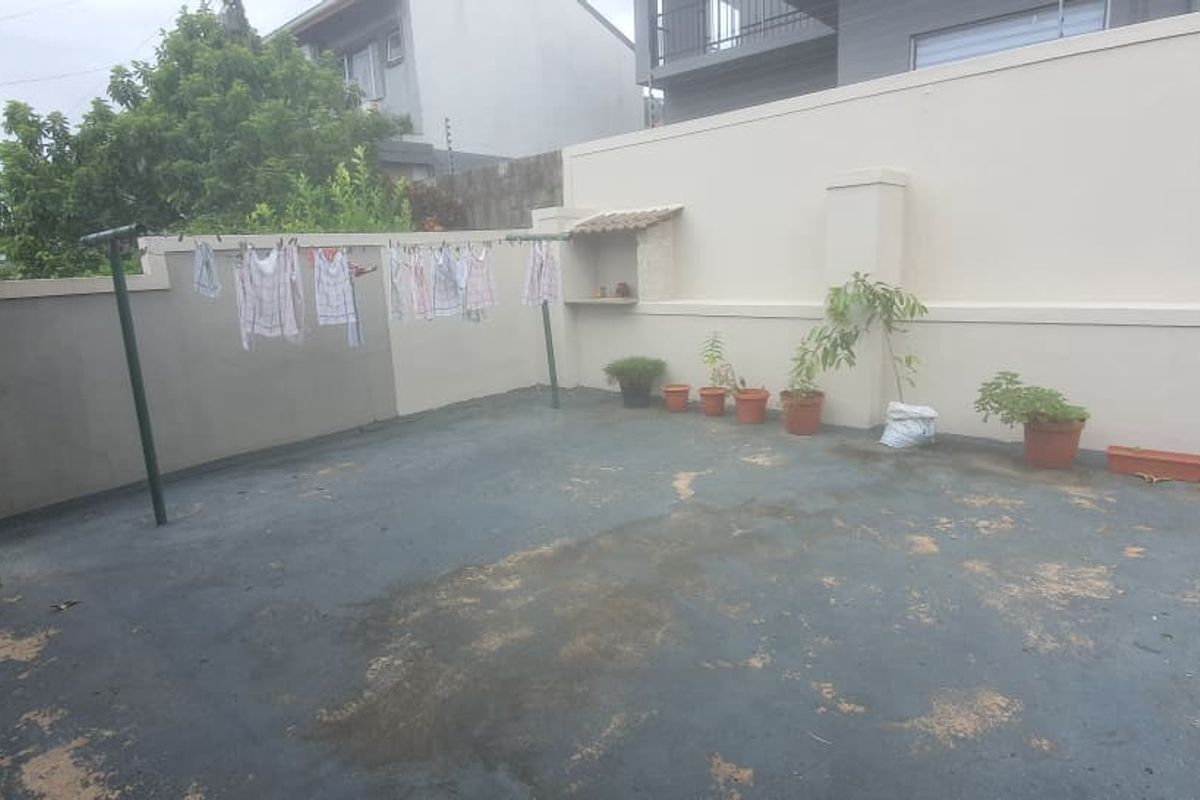 A rear outdoor courtyard area featuring a paved surface, boundary walls, and a small built-in wall niche.