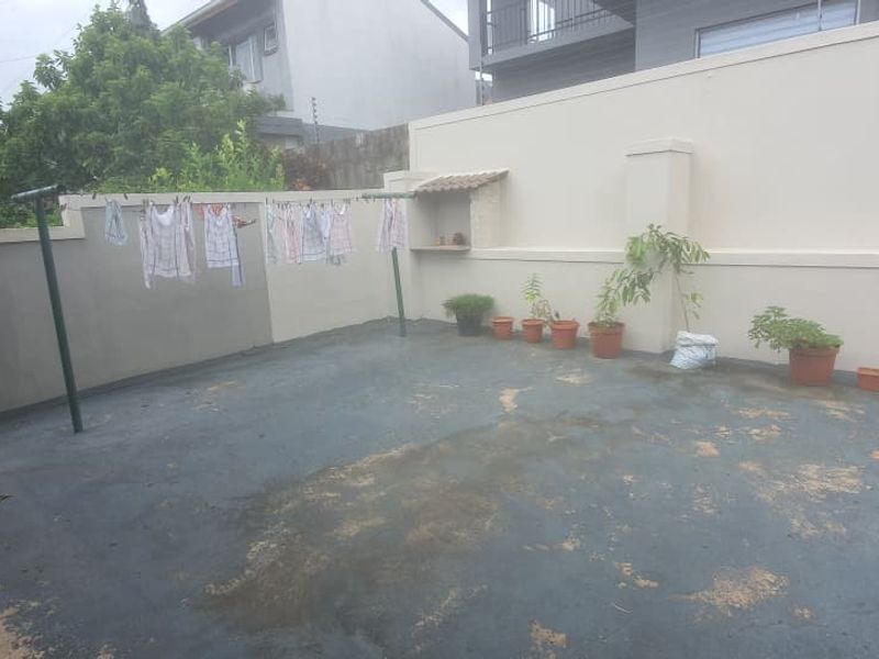A rear outdoor courtyard area featuring a paved surface, boundary walls, and a small built-in wall niche.