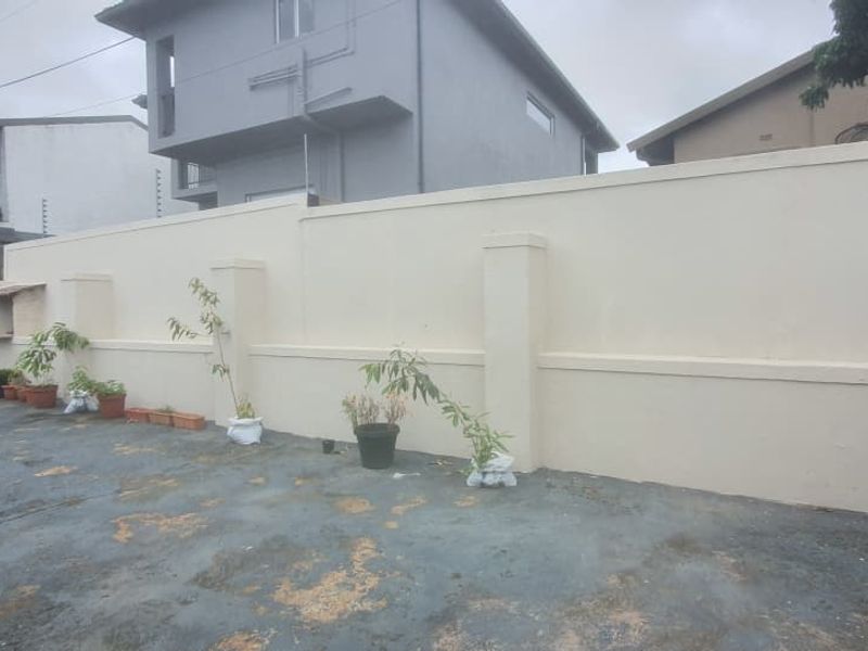 A rear outdoor area featuring a high perimeter boundary wall and extensive concrete paving in need of maintenance.