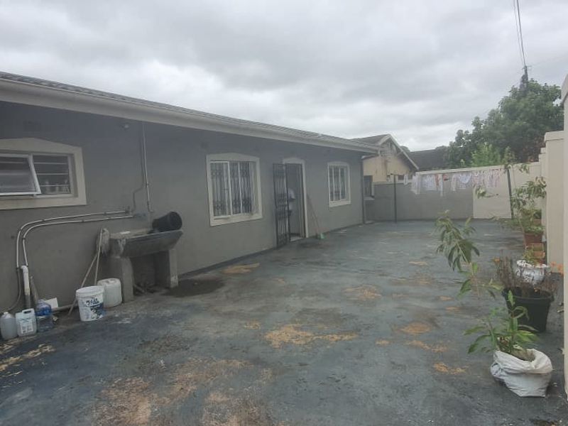 Rear exterior courtyard featuring a concrete wash basin, security bars on windows, and a paved surface enclosed by a perimeter wall.