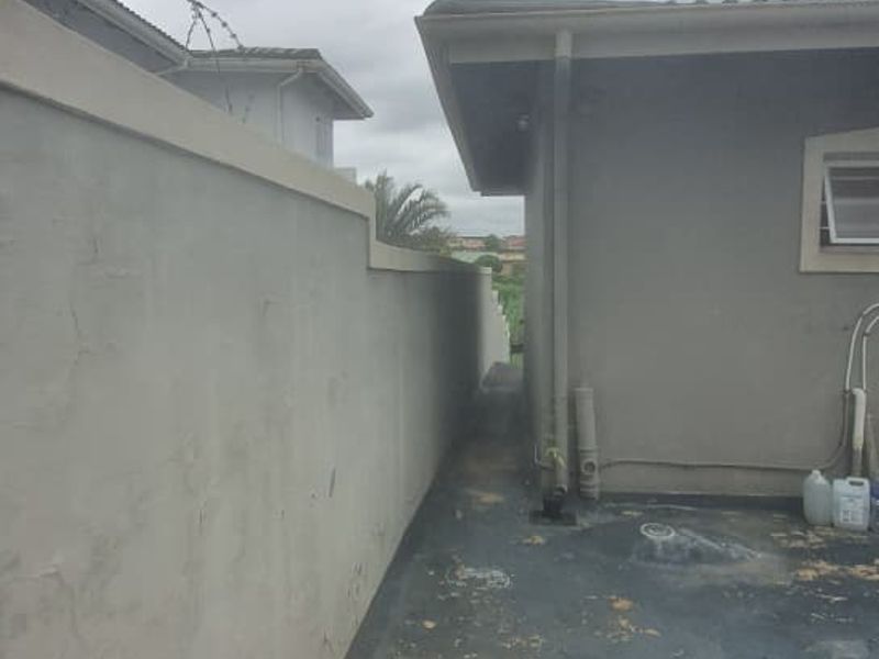 A narrow side passage of the property featuring a boundary wall with security razor wire and weathered paving.