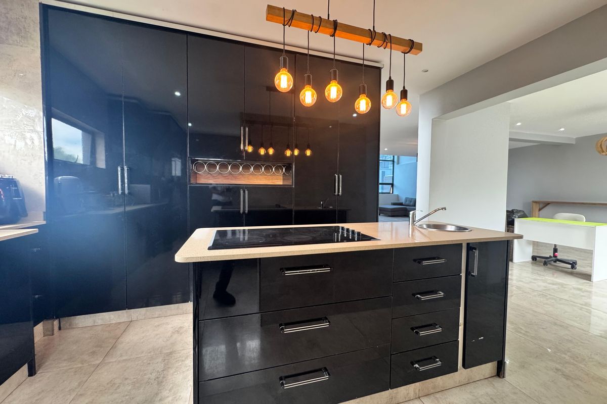 Modern kitchen featuring high-gloss black cabinetry, a central island with an integrated induction hob and sink, and stylish pendant lighting.
