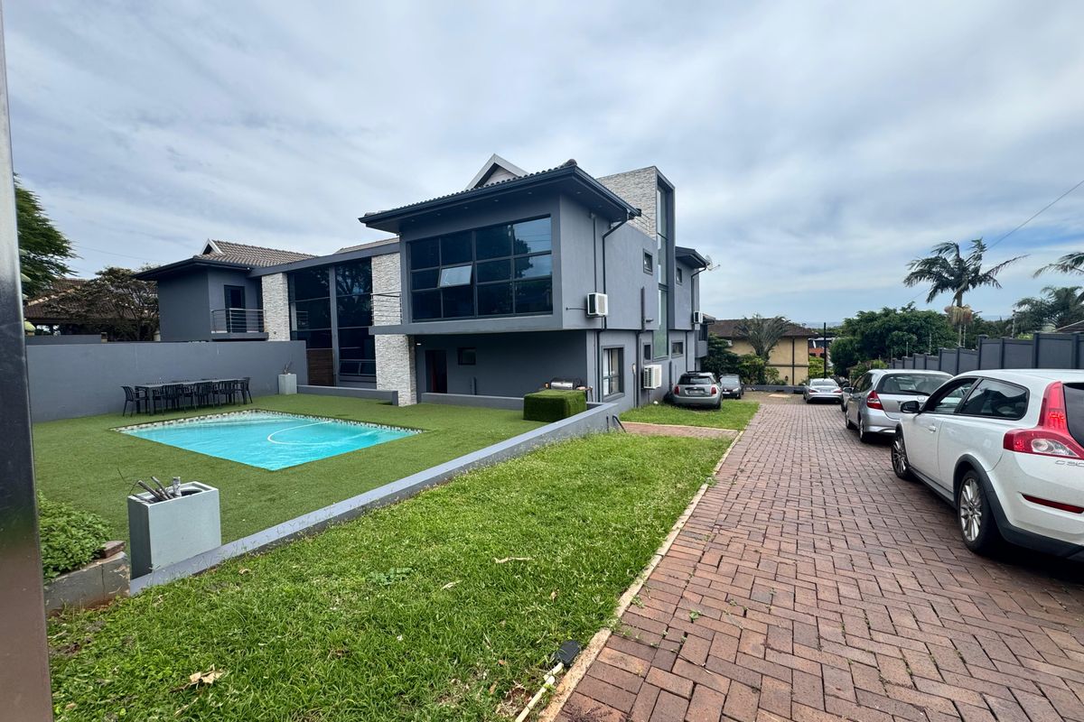 Modern multi-story residence featuring a paved driveway, swimming pool, and landscaped lawn area with contemporary grey exterior finishes.