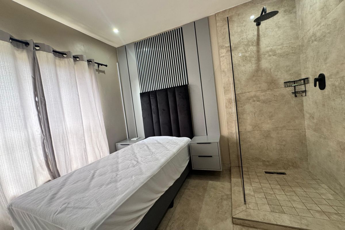 Modern bedroom featuring an integrated open-plan shower area with glass partition, contemporary wall paneling, and neutral floor tiling.