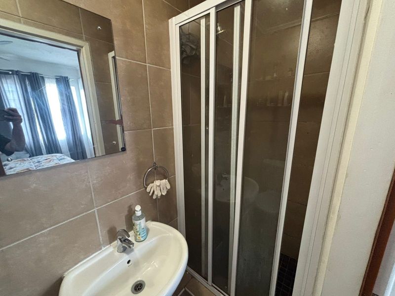 A functional bathroom featuring a pedestal washbasin, wall-mounted mirror, and a glass-enclosed shower with tiled wall and floor finishes.