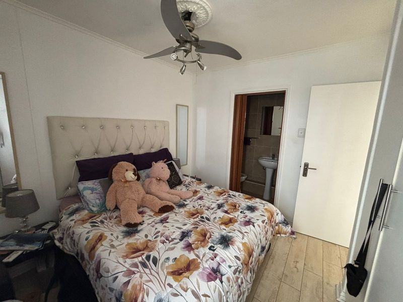 A bedroom featuring tiled flooring, a ceiling fan with decorative rose, and an adjoining en-suite bathroom with a pedestal basin.