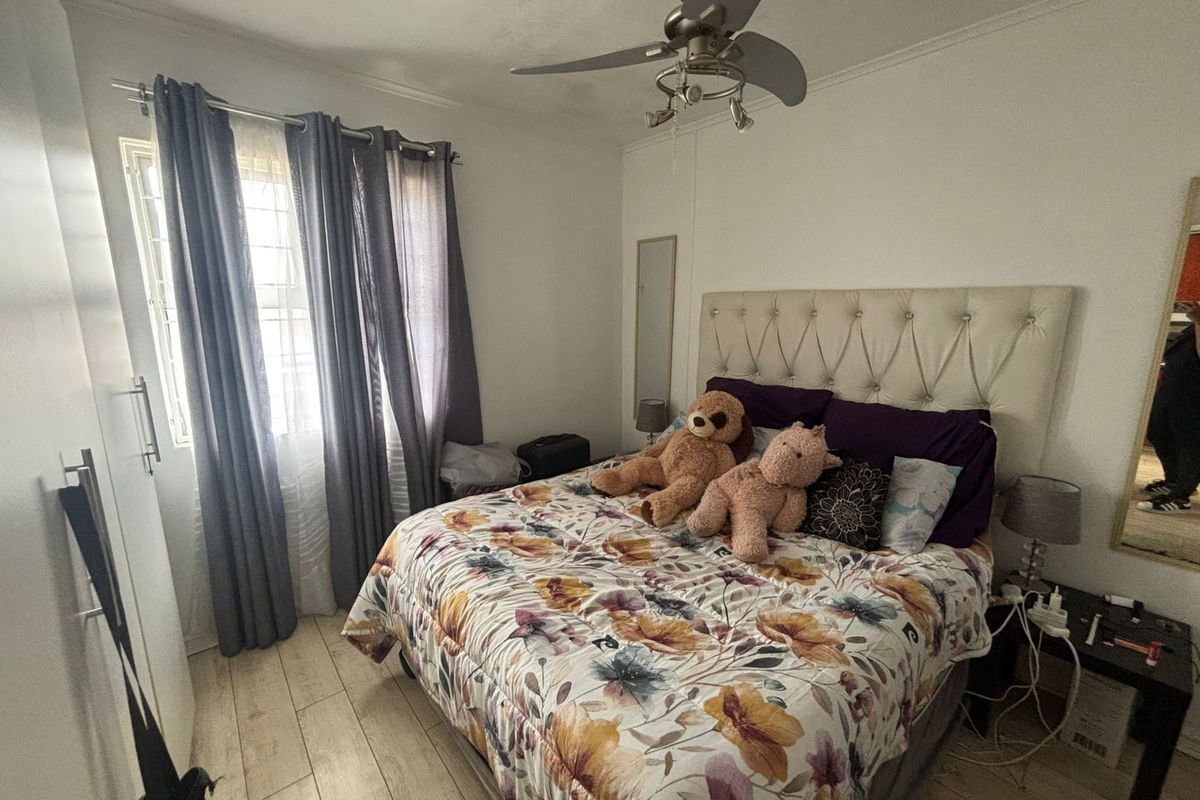 A functional bedroom featuring tiled flooring, a ceiling fan, and a built-in wardrobe with security bars on the window.