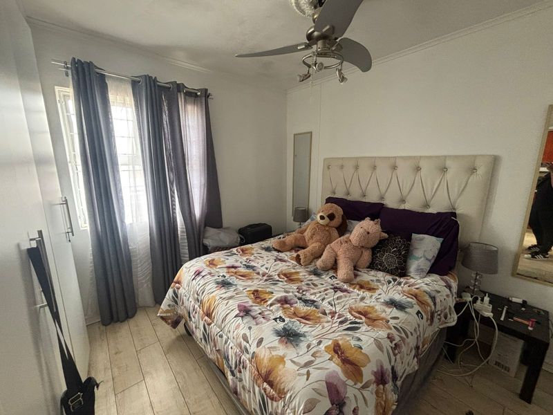 A functional bedroom featuring tiled flooring, a ceiling fan, and a built-in wardrobe with security bars on the window.