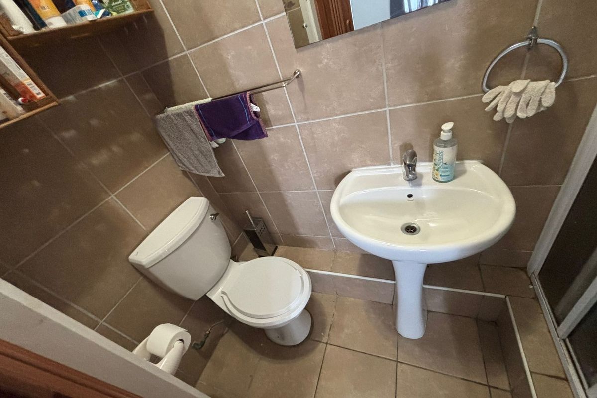 A compact bathroom featuring a pedestal washbasin, toilet, and neutral wall and floor tiling.