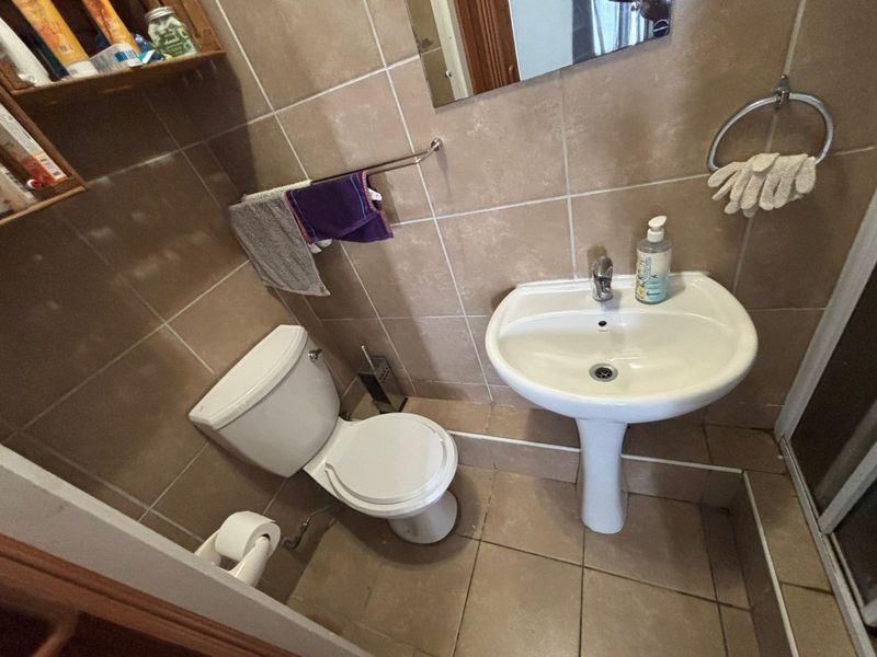 A compact bathroom featuring a pedestal washbasin, toilet, and neutral wall and floor tiling.
