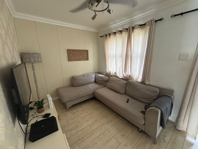 A cozy living room featuring light-toned laminate flooring, crown molding, and a ceiling fan, providing a comfortable and functional space.