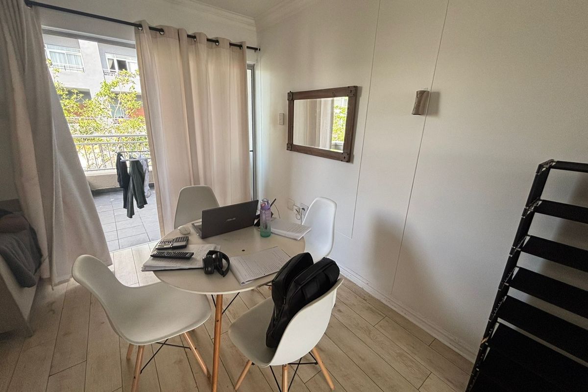 A bright living area featuring light-toned laminate flooring and direct access to a private balcony through a sliding glass door.