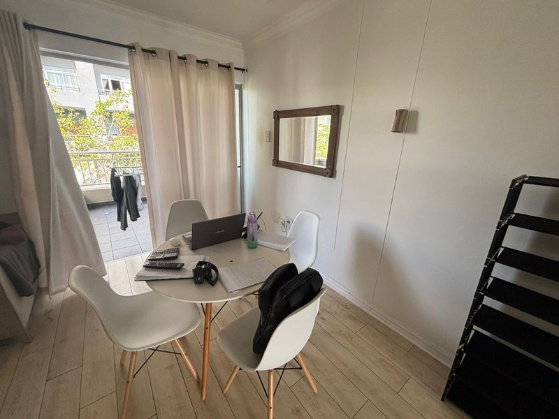 A bright living area featuring light-toned laminate flooring and direct access to a private balcony through a sliding glass door.