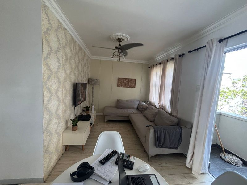 A living room featuring laminate flooring, decorative wallpaper, and a ceiling fan with a central rose, providing a comfortable and functional living space.