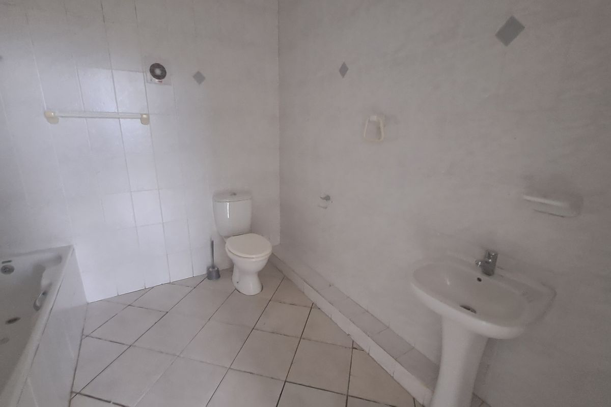 A functional bathroom featuring a bathtub, pedestal basin, and toilet with neutral wall and floor tiling.