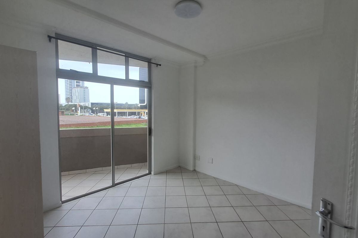 An empty bedroom featuring tiled flooring, a built-in cupboard, and a sliding glass door providing access to a private balcony.