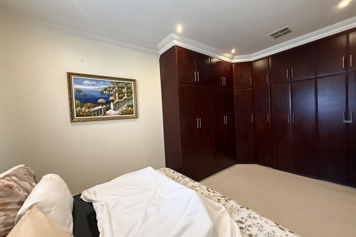 A well-maintained bedroom featuring extensive dark wood built-in cabinetry providing ample storage space, complemented by recessed ceiling lighting and crown molding.