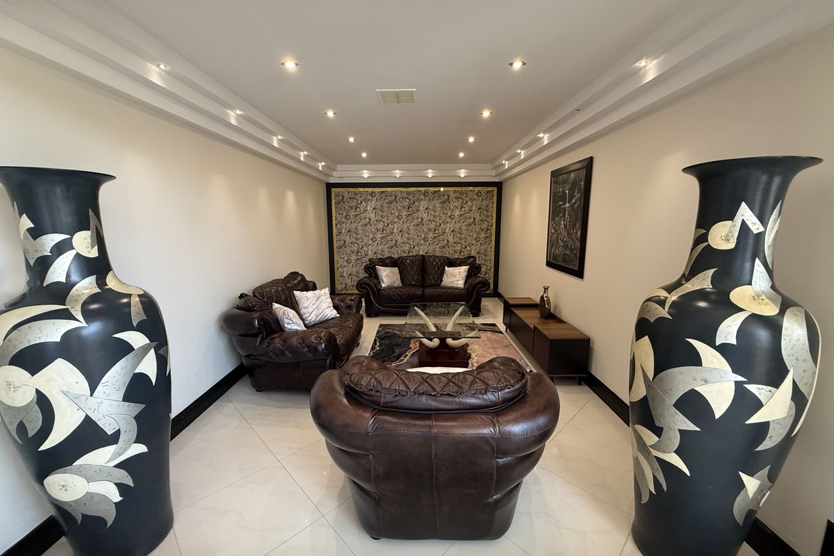 A well-maintained living room featuring recessed ceiling lighting, decorative wall paneling, and polished tile flooring.