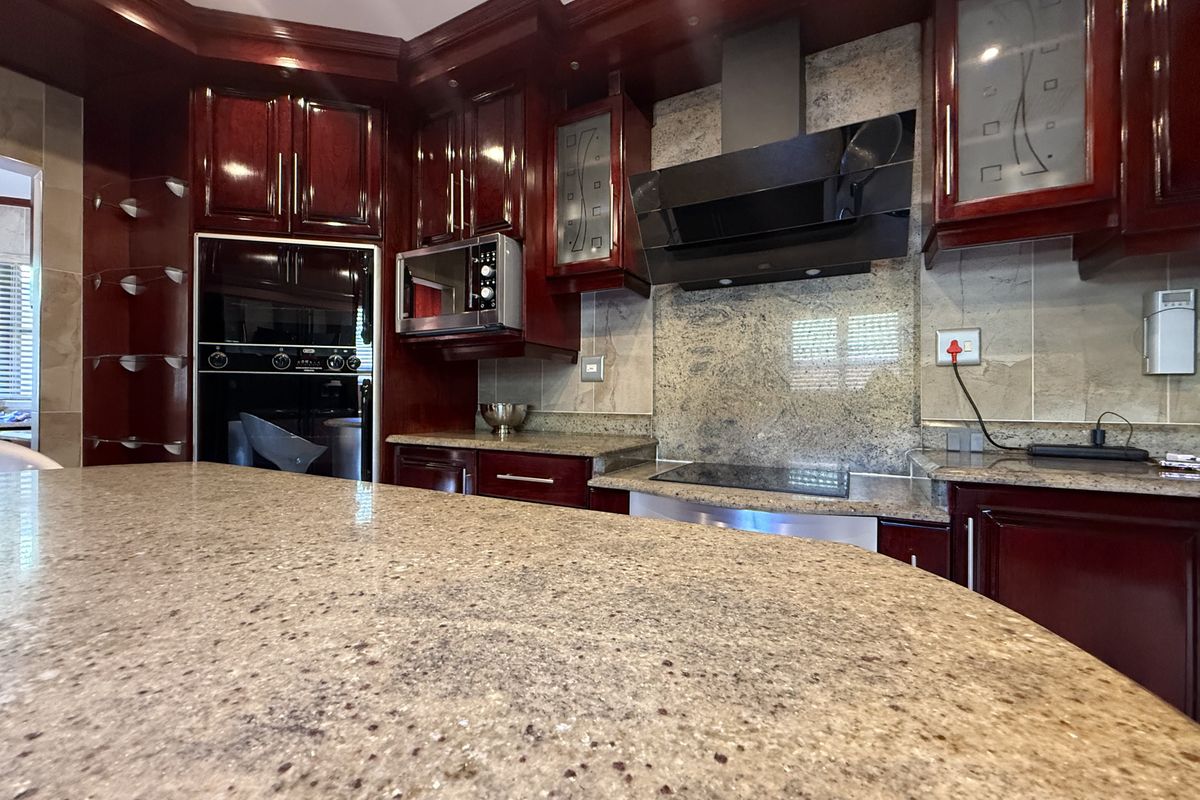 A well-appointed kitchen featuring dark wood cabinetry, granite countertops, a built-in oven, microwave, and a modern extractor fan over the cooktop.