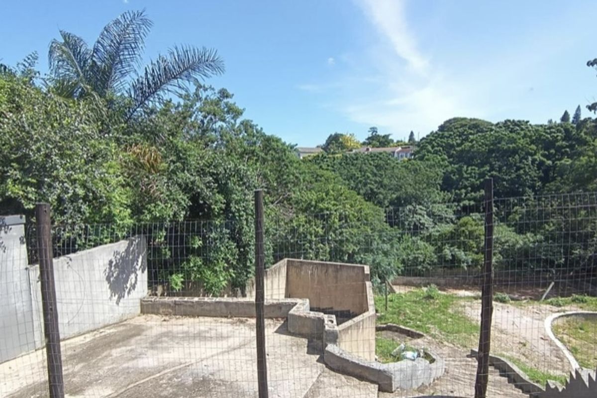 An outdoor area featuring concrete retaining walls and tiered levels, overlooking a lush green valley with mature trees and natural vegetation.