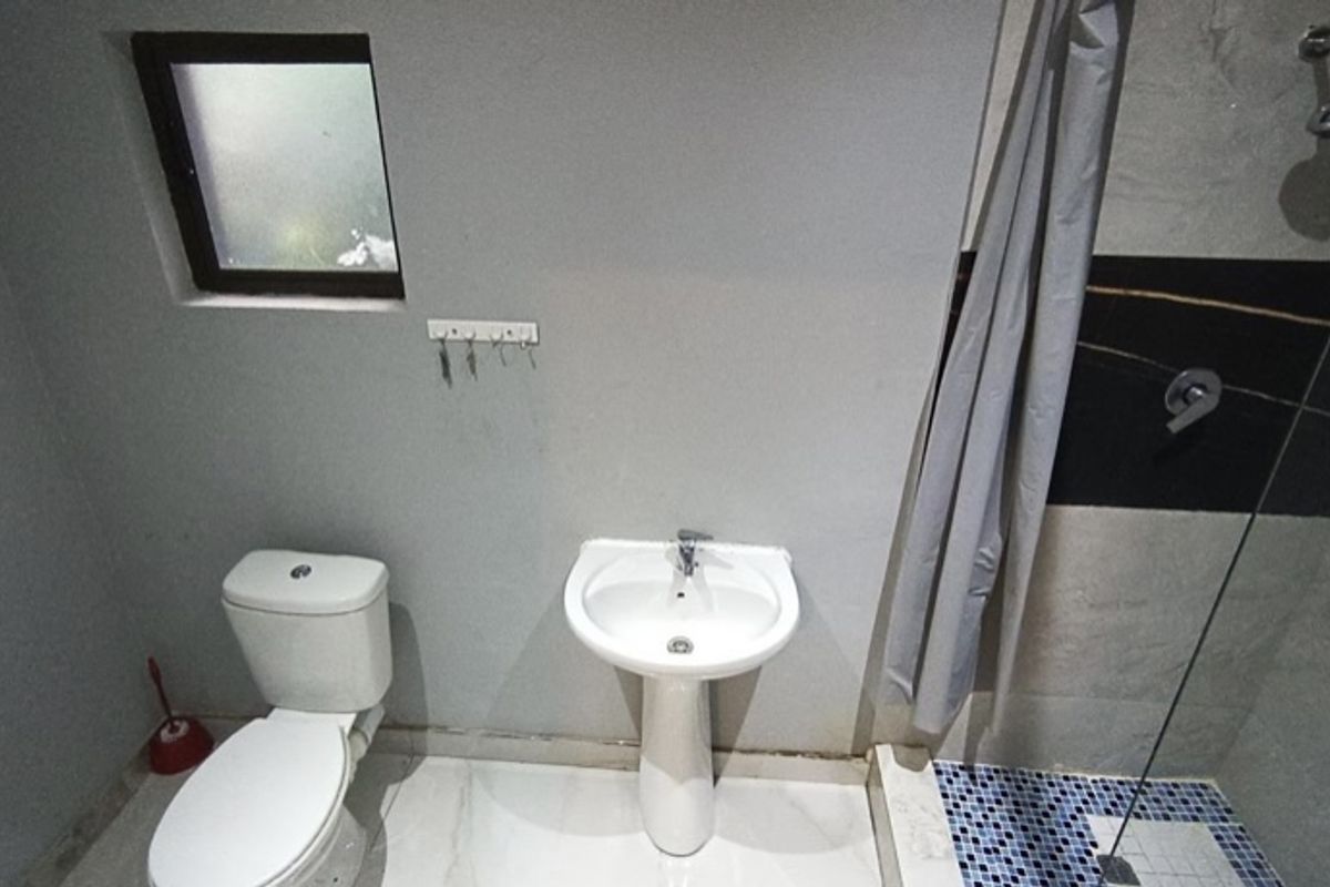 A functional bathroom featuring a pedestal basin, a toilet, and a shower enclosure with mosaic floor tiling.