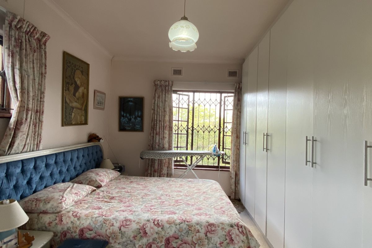 A bedroom featuring built-in floor-to-ceiling wardrobes and a window with security bars, providing ample storage and natural light.