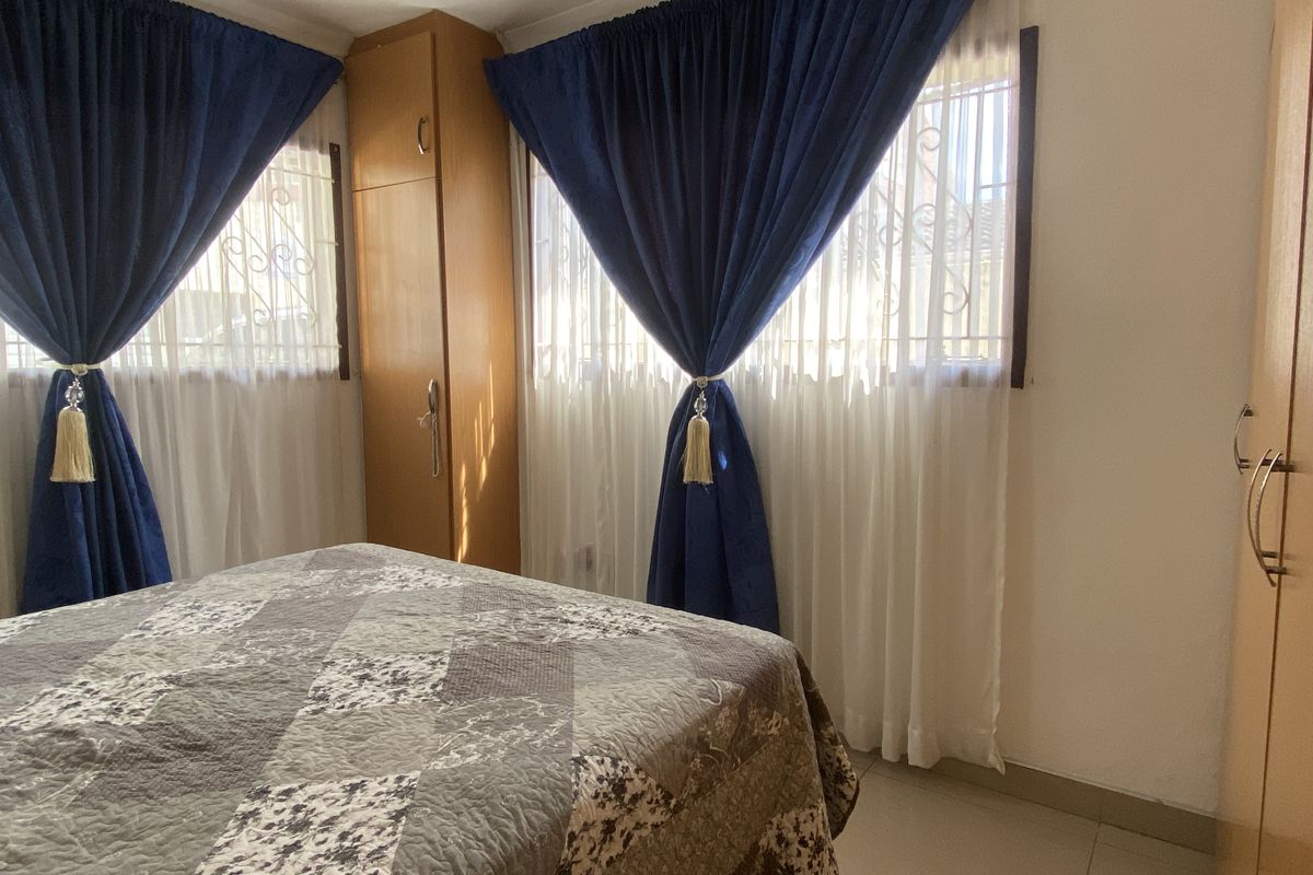 A bedroom featuring built-in wooden cupboards and tiled flooring, with security bars installed on the windows.