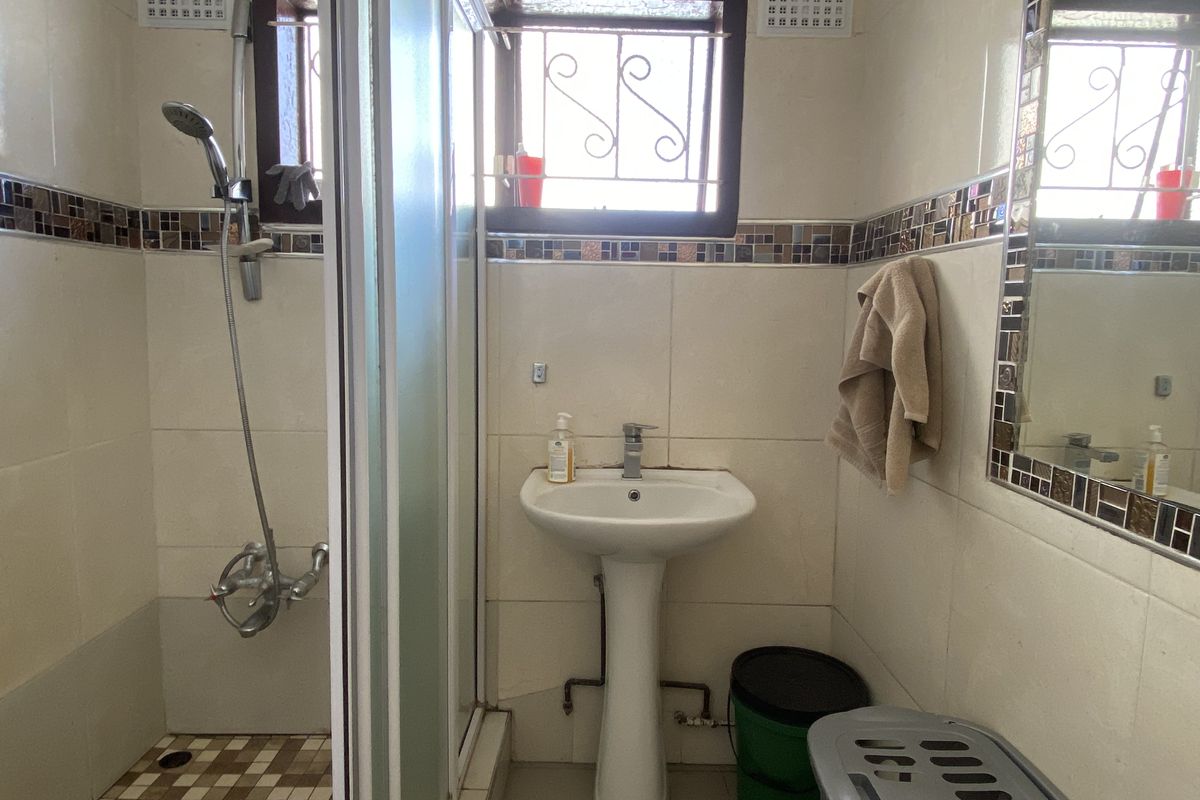 A functional bathroom featuring a pedestal basin, a glass-enclosed shower, and decorative mosaic tile accents.