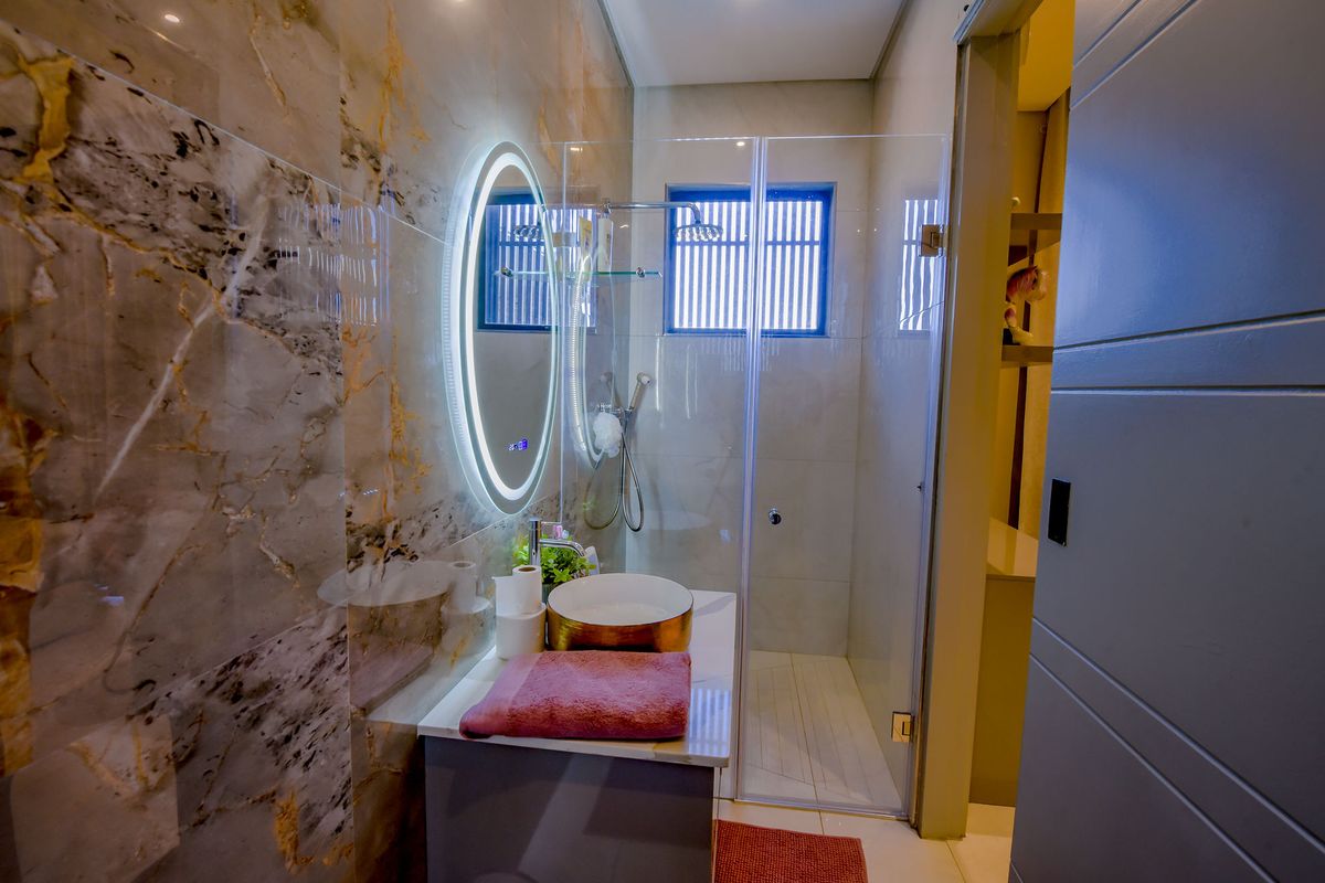 Modern bathroom featuring marble-look wall tiles, a vessel sink vanity, a backlit circular mirror, and a glass-enclosed shower with a rainfall showerhead.