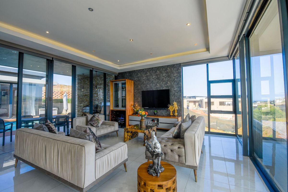 Modern open-plan living area featuring large floor-to-ceiling glass sliding doors, recessed ceiling lighting, and tiled flooring with seamless indoor-outdoor flow.