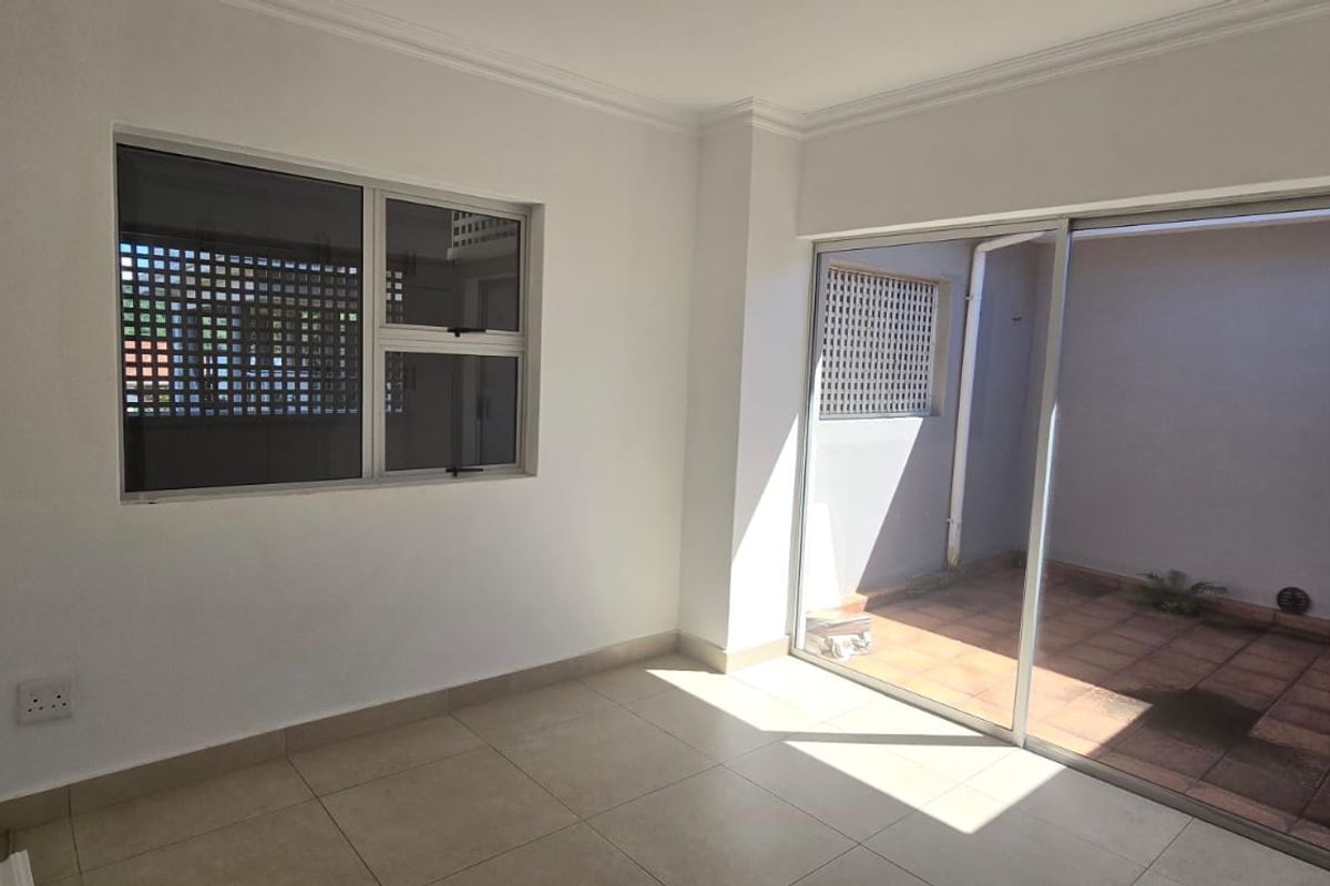 A bright, empty living area featuring neutral floor tiles, large sliding glass doors leading to a private patio, and a window with security bars.