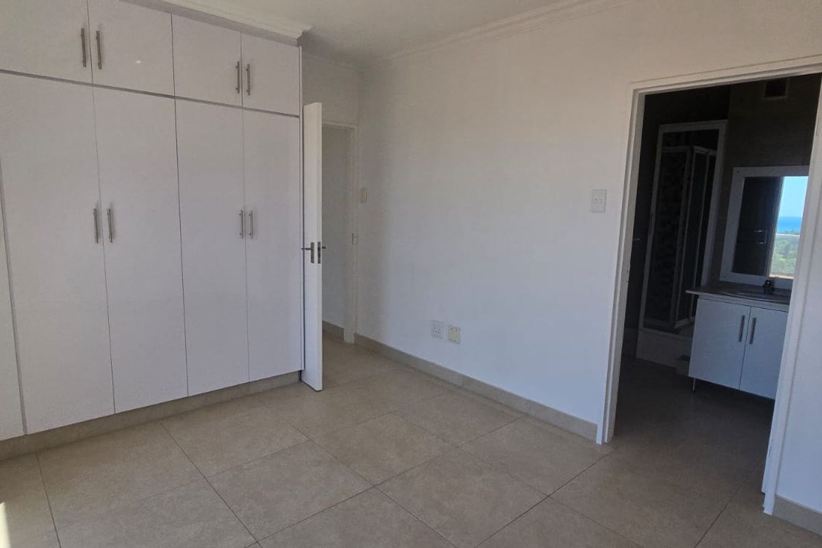 A bright bedroom featuring built-in white cabinetry, tiled flooring, and direct access to an en-suite bathroom.