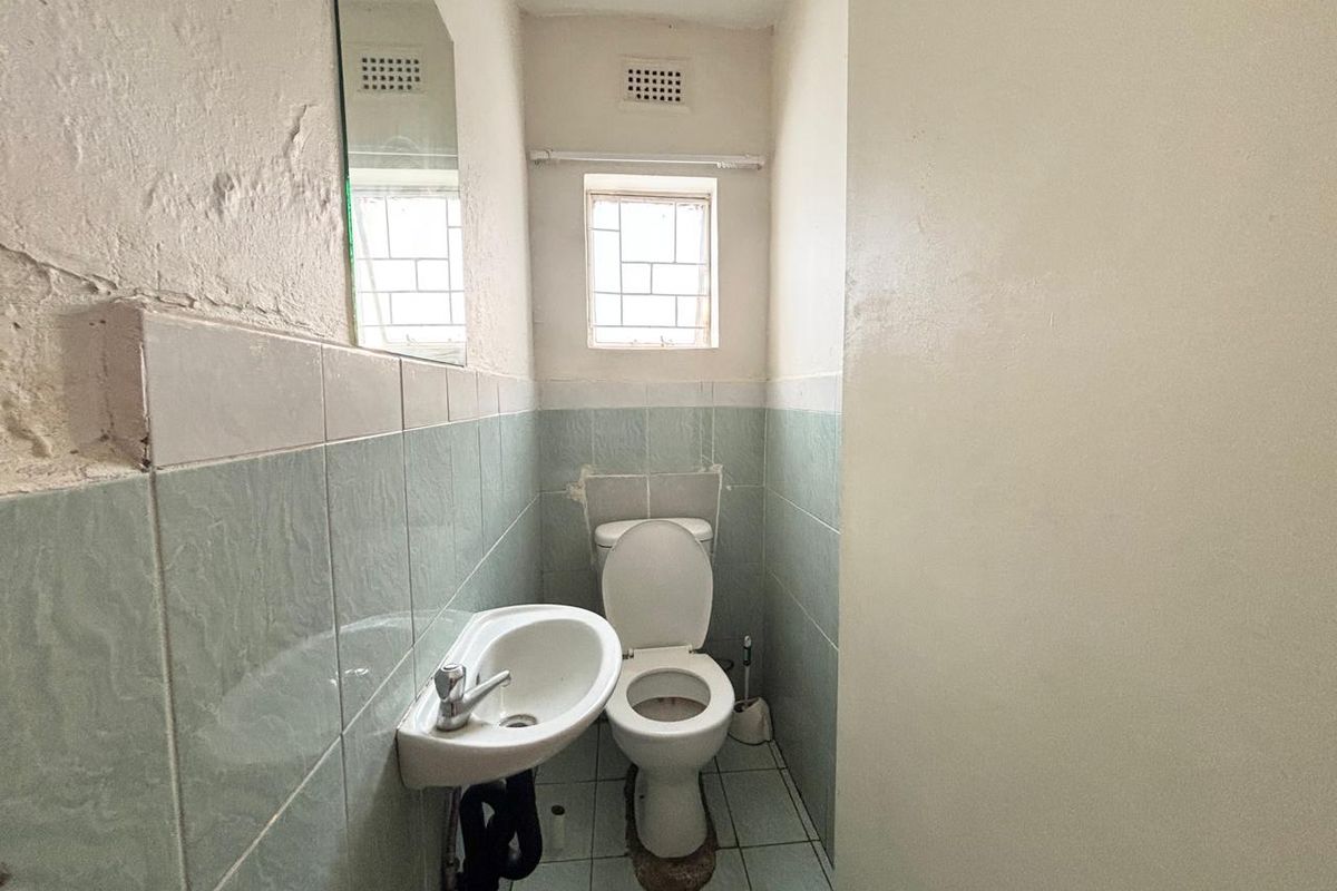 A compact, dated bathroom featuring a wall-mounted basin and toilet, with tiled walls and floor, requiring cosmetic updates and repairs.