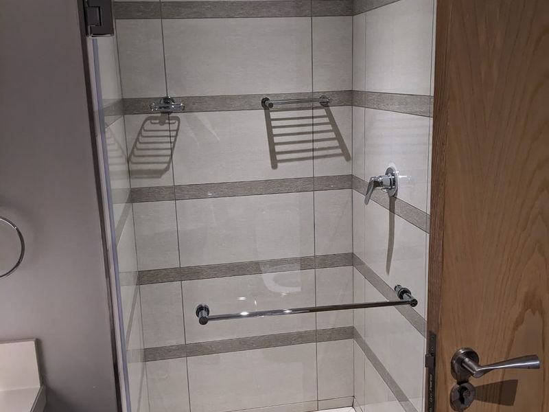 A modern walk-in shower featuring tiled walls with decorative accents, a glass enclosure, a fixed shower head, and chrome fixtures.