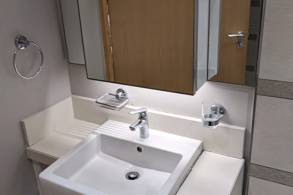 A modern bathroom vanity featuring a wall-mounted basin, integrated cabinetry, and a large mirror with built-in lighting.