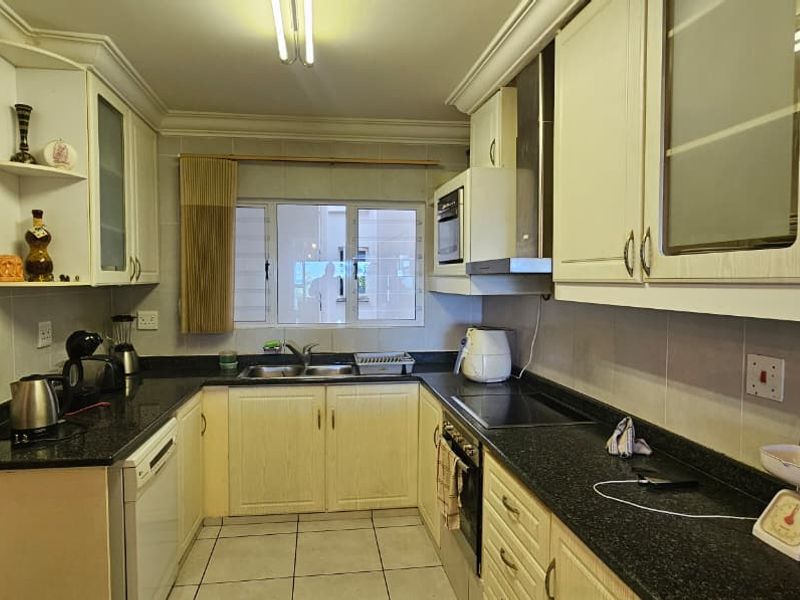 A functional galley-style kitchen featuring dark granite countertops, light-toned cabinetry, integrated oven, hob, and extractor fan with tiled flooring.