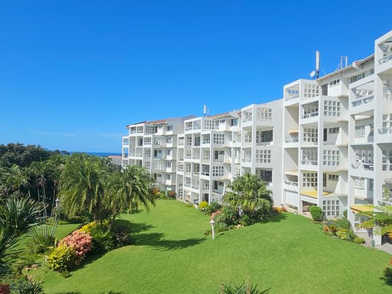 Elevated view of the apartment complex exterior, showcasing the building facade, landscaped garden, and surrounding greenery.
