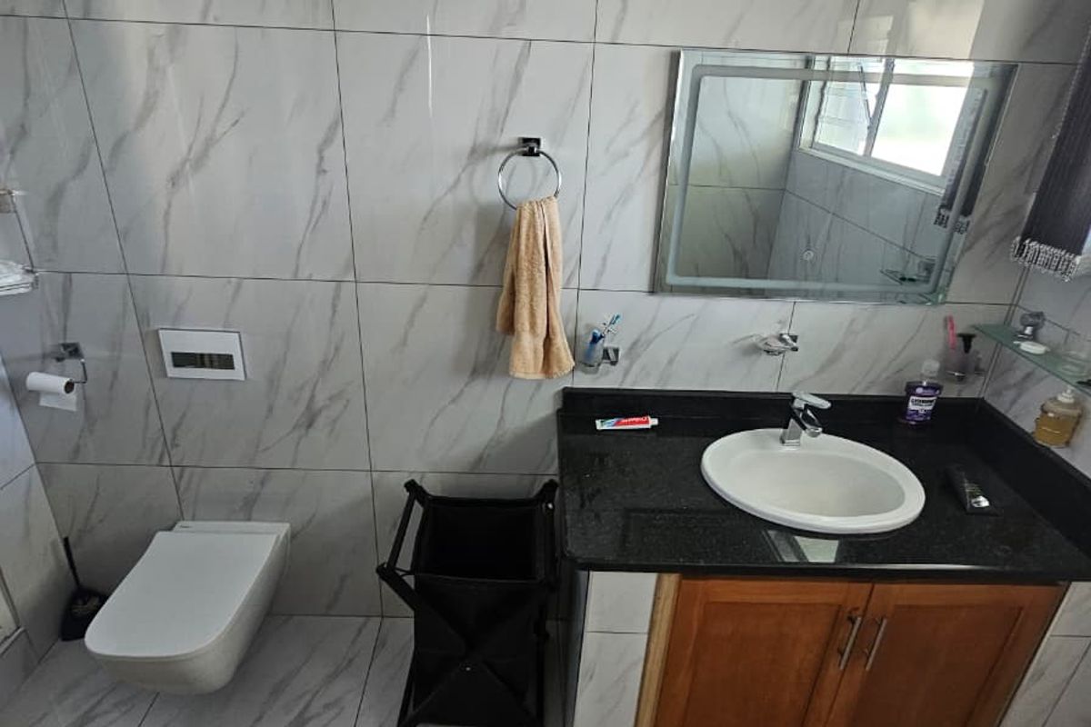Modern bathroom featuring marble-look wall tiles, a wall-mounted toilet, a dark granite vanity countertop with an integrated basin, and a backlit mirror.