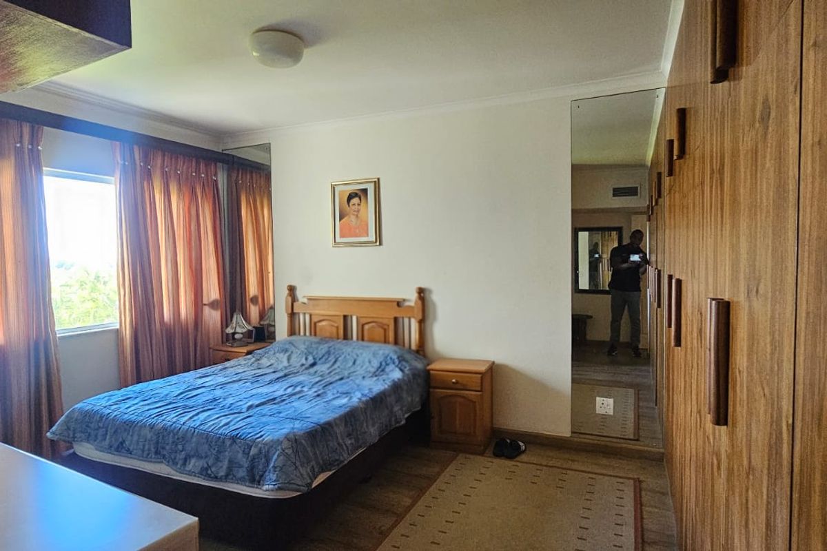 A bedroom featuring extensive built-in wooden cabinetry with integrated mirror panels and large windows with curtains.
