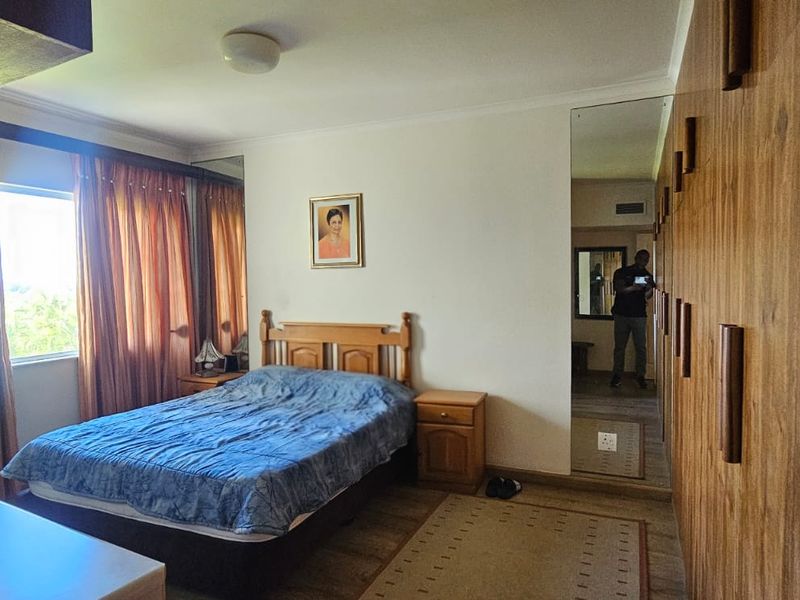 A bedroom featuring extensive built-in wooden cabinetry with integrated mirror panels and large windows with curtains.