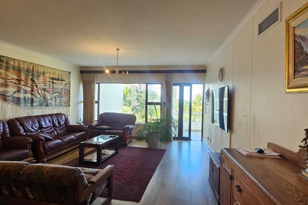 Spacious living room featuring wood-look flooring, recessed ceiling lighting, and large glass sliding doors providing access to an outdoor balcony area.