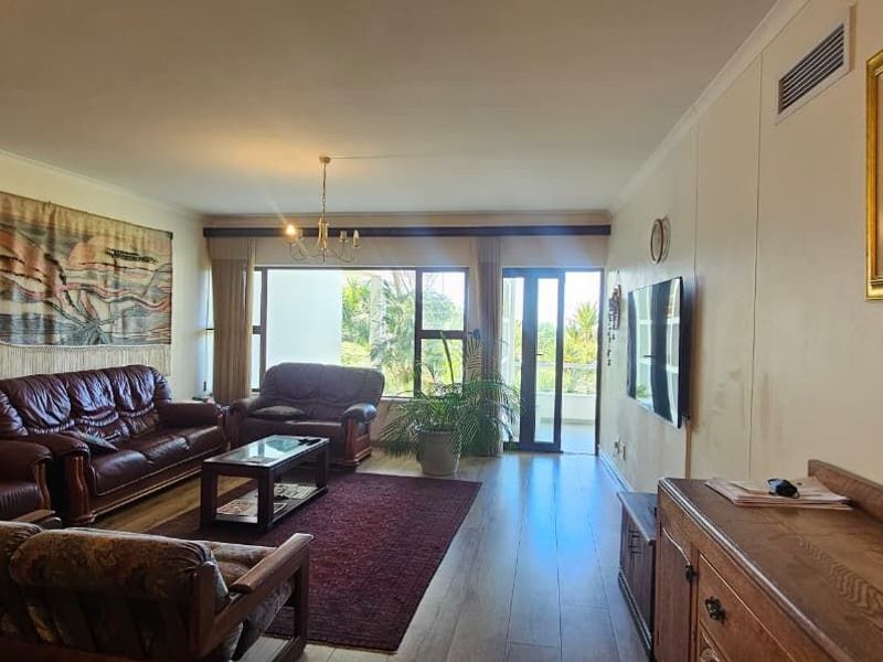 Spacious living room featuring wood-look flooring, recessed ceiling lighting, and large glass sliding doors providing access to an outdoor balcony area.