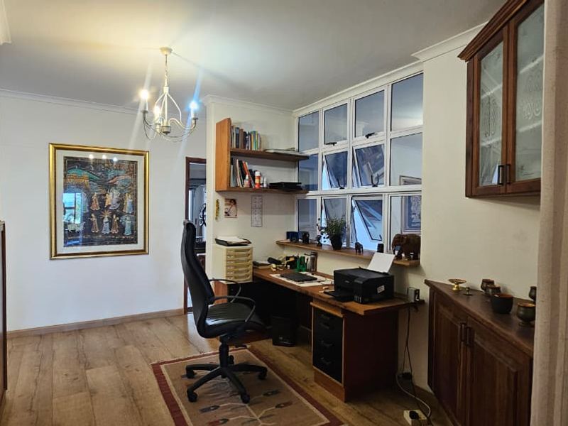 A functional home office space featuring built-in wooden cabinetry, shelving, and large windows providing natural light.