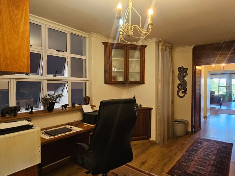 A functional home office space featuring built-in wooden cabinetry, a window with natural light, and wood-look flooring, leading into an adjacent living area.