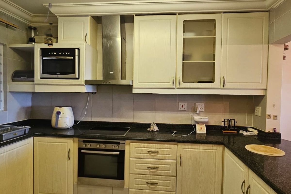 A functional kitchen featuring granite countertops, built-in oven, electric hob, stainless steel extractor fan, and ample cabinetry for storage.