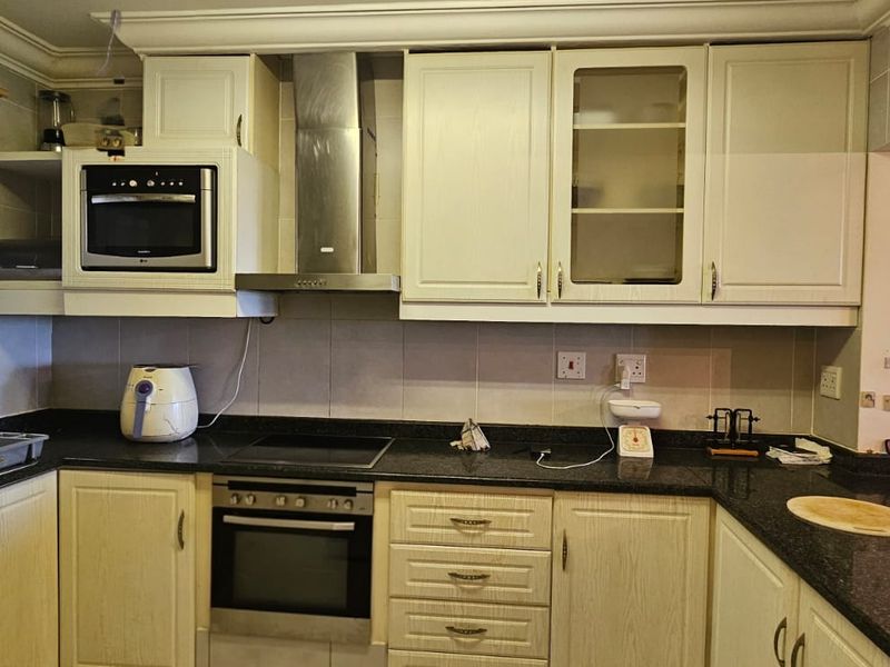 A functional kitchen featuring granite countertops, built-in oven, electric hob, stainless steel extractor fan, and ample cabinetry for storage.