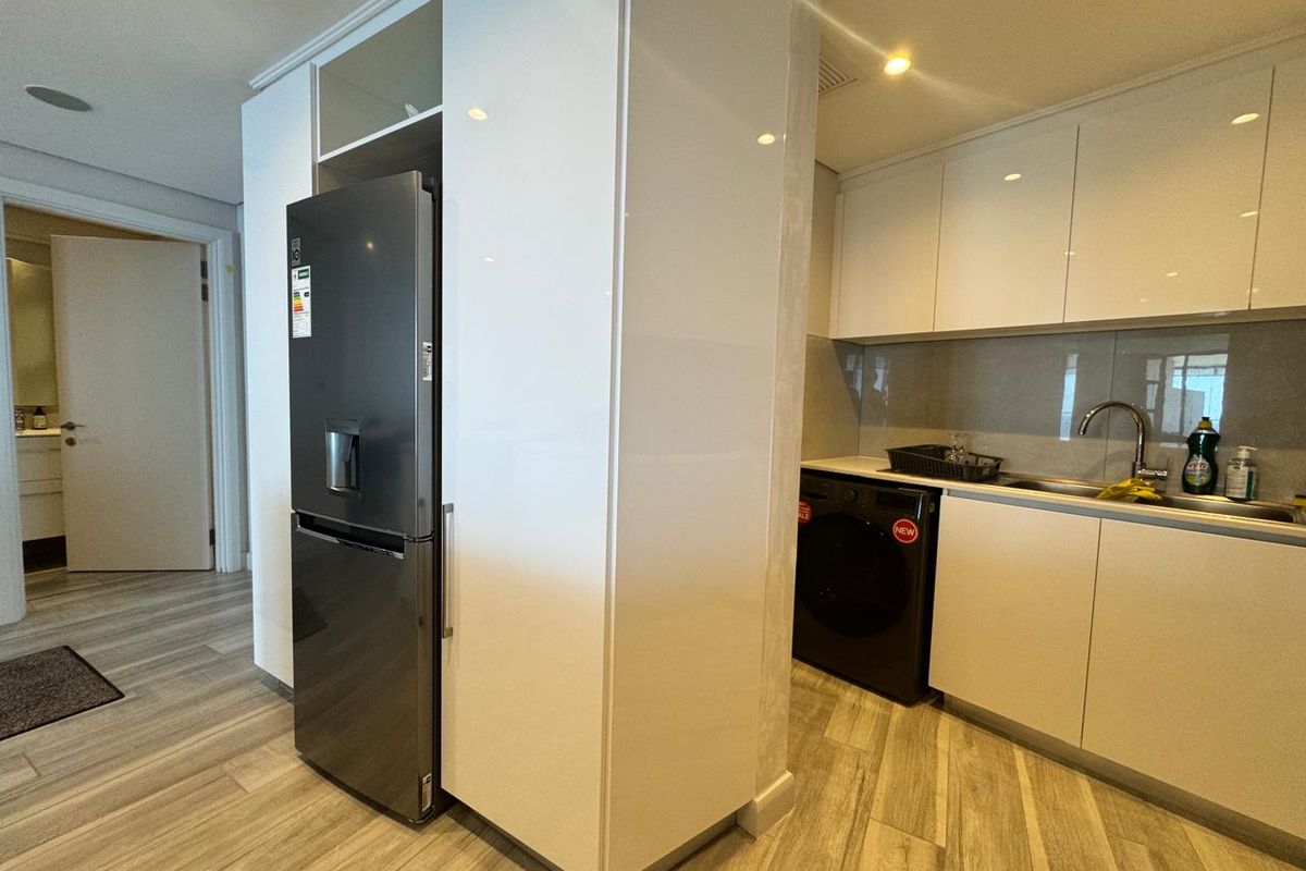 Modern kitchen featuring sleek white cabinetry, integrated storage, and wood-look flooring, seamlessly connected to the living area.