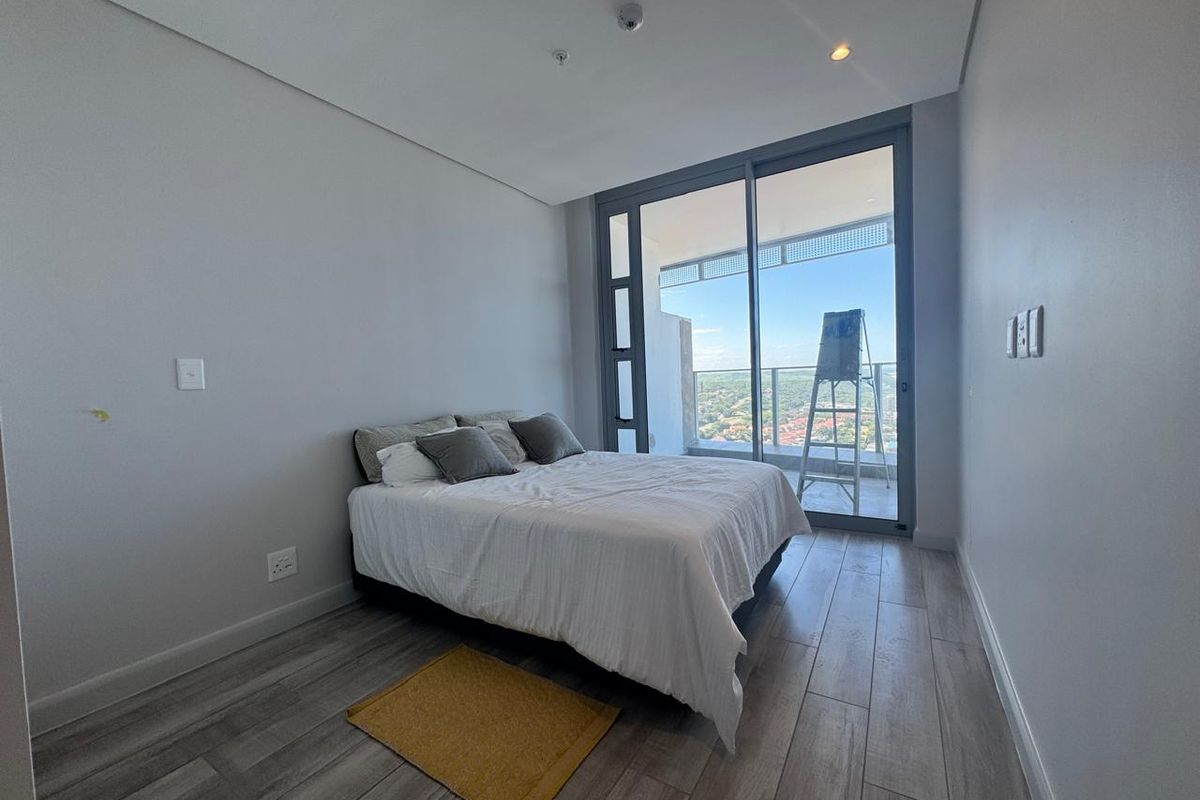 Modern bedroom featuring wood-look tile flooring, neutral walls, and large sliding glass doors opening to a private balcony with expansive views.