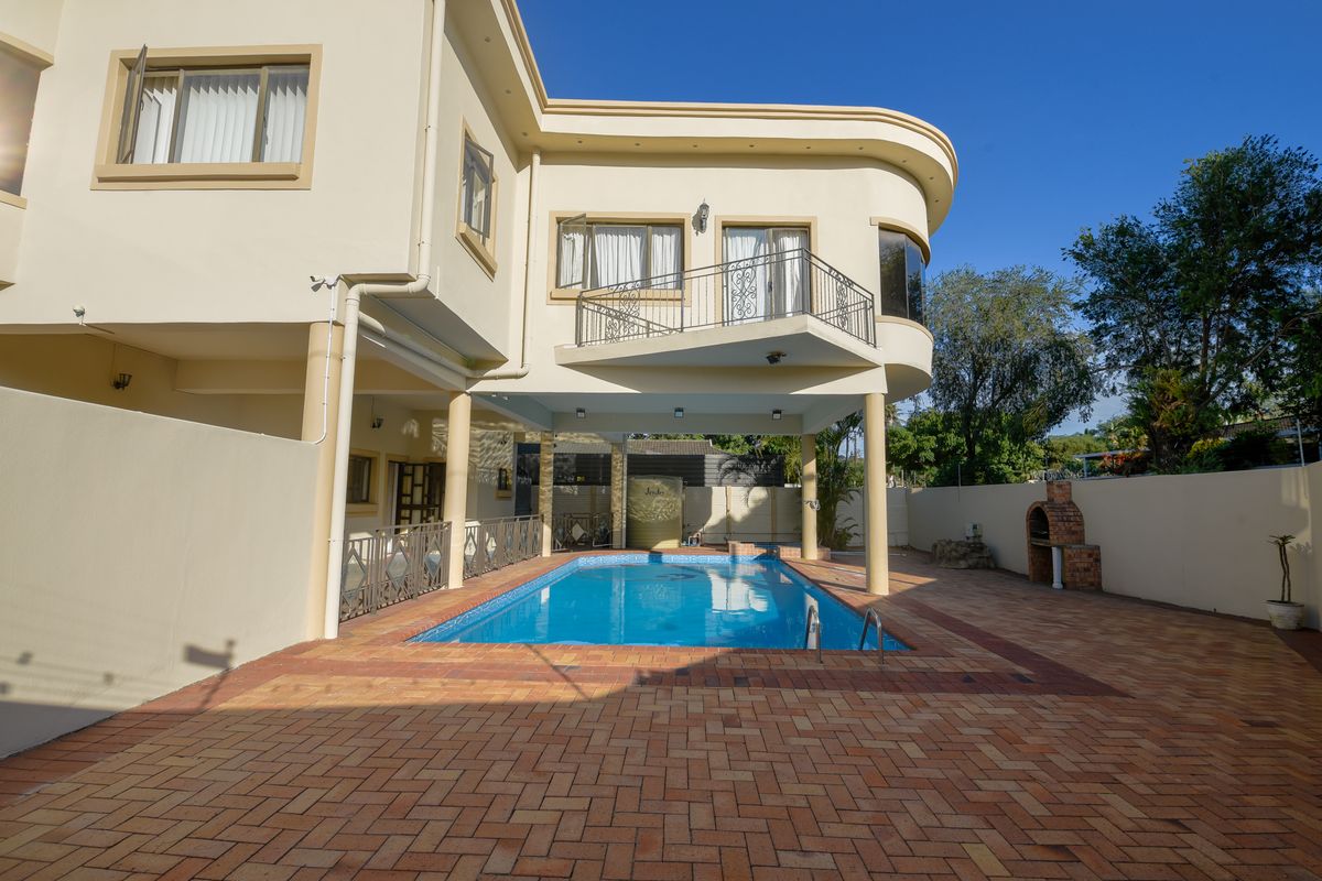 Rear view of the property featuring a swimming pool, paved patio area, built-in brick braai, and a covered balcony on the upper level.