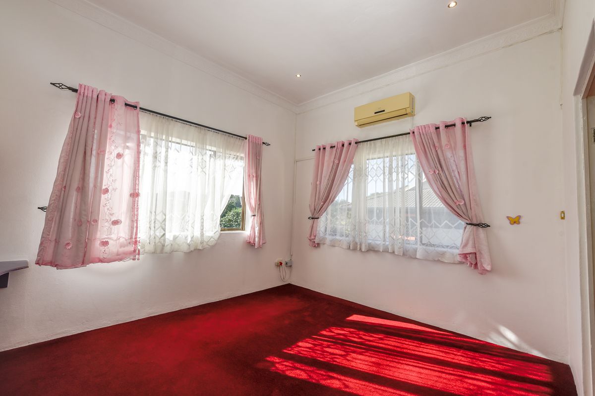 A bright bedroom featuring red carpeting, dual windows with curtain rods, and a wall-mounted air conditioning unit.